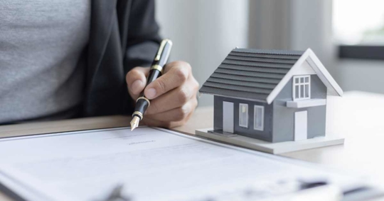 miniature house beside a person signing a document